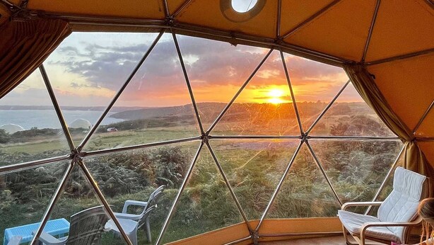 Een geodetische koepel met een panoramisch uitzicht op een zonsondergang boven een glooiend landschap.