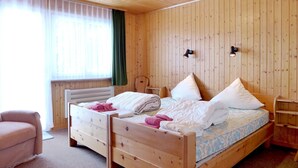 Et soveværelse med træpaneler, en seng, to sengeborde, en stol og en radiator.