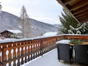 Ein Balkon mit Holzgeländer, Tisch und Stühlen mit Blick auf eine verschneite Berglandschaft.