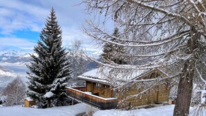 En træhytte med balkon, omgivet af sneklædte træer og bjerge i baggrunden.
