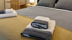 Ein ordentlich bezogenes Bett mit grauer Bettwäsche, ein Holzschrank, eine Nachttischlampe und ein Bild an der Wand.