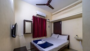 A bedroom with a bed, a ceiling fan, an air conditioner, a TV, a bedside table, a mirror, a window with curtains, and a sink. - Puducherry Residency (Puducherry)