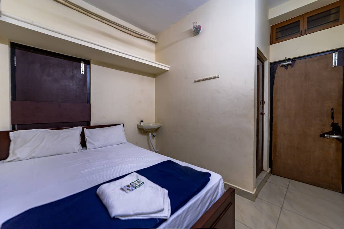 A hotel room with a bed, a bedside table, a wall-mounted shelf, and a door.