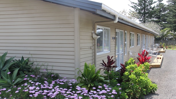 Un motel con una hilera de habitaciones, un camino de grava y un jardín con diversas plantas y flores.