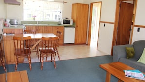 Cocina compacta con armarios de madera, un microondas y un lavabo. Hay una mesa de comedor con sillas y un sofá en la zona de estar.