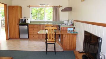 A compact kitchen with a microwave, refrigerator, wooden cabinets, a sink, and a dining area with a chair.