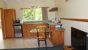 Una cocina compacta con armarios de madera, un microondas, un lavamanos y una ventana con cortinas.