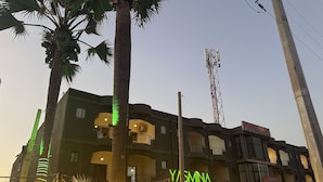 Ein mehrstöckiges Gebäude mit Balkonen, einer Bar namens "Y/ASMINA ESTO BAR" und einem Schild mit der Aufschrift "SALLY'S 24 World".