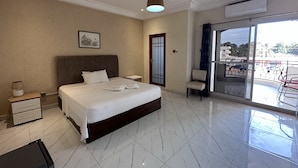 Ein Hotelzimmer mit einem großen Bett, einem Nachttisch, einem Sessel, einem Balkon mit Aussicht und einer Deckenleuchte.