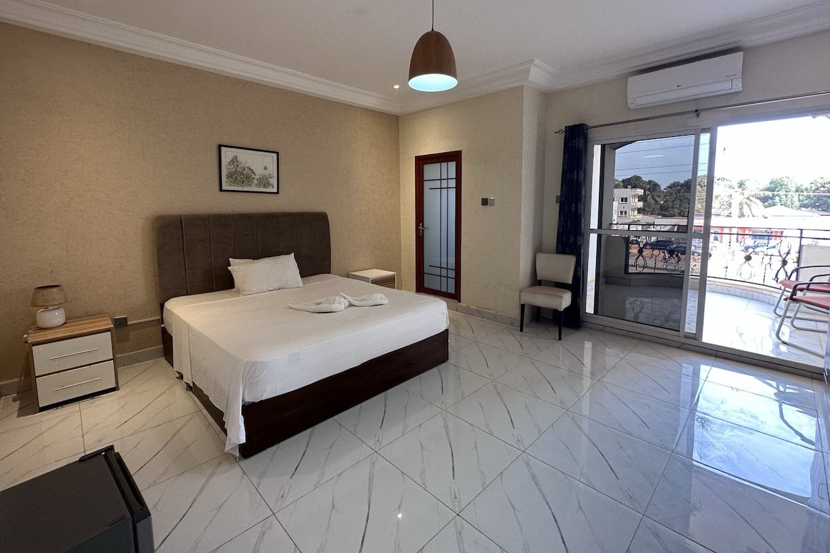 Habitación de hotel con una cama grande, una mesita de noche, una silla, un balcón con vistas y una lámpara en el techo.
