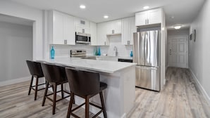 A modern kitchen with white cabinets, a stainless steel refrigerator, and a central island with bar stools. - La Mirage Condo 237 Beachfront Resort Condominiums with Private Boardwalk (Port Aransas)