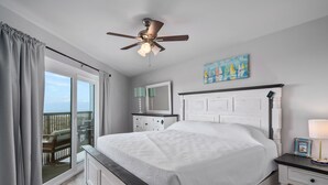A bedroom with a bed, a nightstand, a ceiling fan, a window with curtains, a painting, and a view of the outdoors. - La Mirage Condo 237 Beachfront Resort Condominiums with Private Boardwalk (Port Aransas)