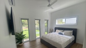 Ein Schlafzimmer mit einem großen Bett, einem Deckenventilator und Blick auf einen Garten durch eine Glasschiebetür.