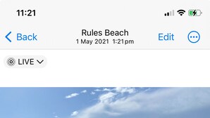 Eine Person spaziert mit einem Hund über einen sandigen Strand, im Hintergrund sind Wellen zu sehen.