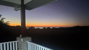 Ein Balkon mit Steinpfeiler und weißer Reling, mit Blick auf einen Sonnenuntergang über dem Wasser.