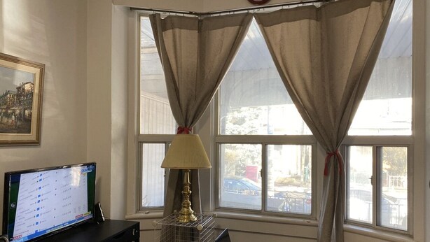 Una habitación con escritorio, computadora, lámpara y dos ventanas con cortinas.