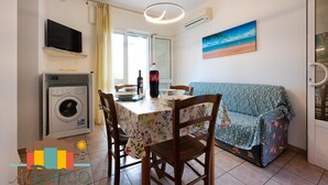 Ett kompakt bostadsutrymme med ett matbord, stolar, en soffa, en tvättmaskin och en tv som är monterad på väggen.
