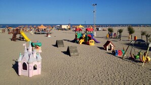 Ein Strand mit Spielgeräten, Sonnenschirmen und einem Rettungsturm.