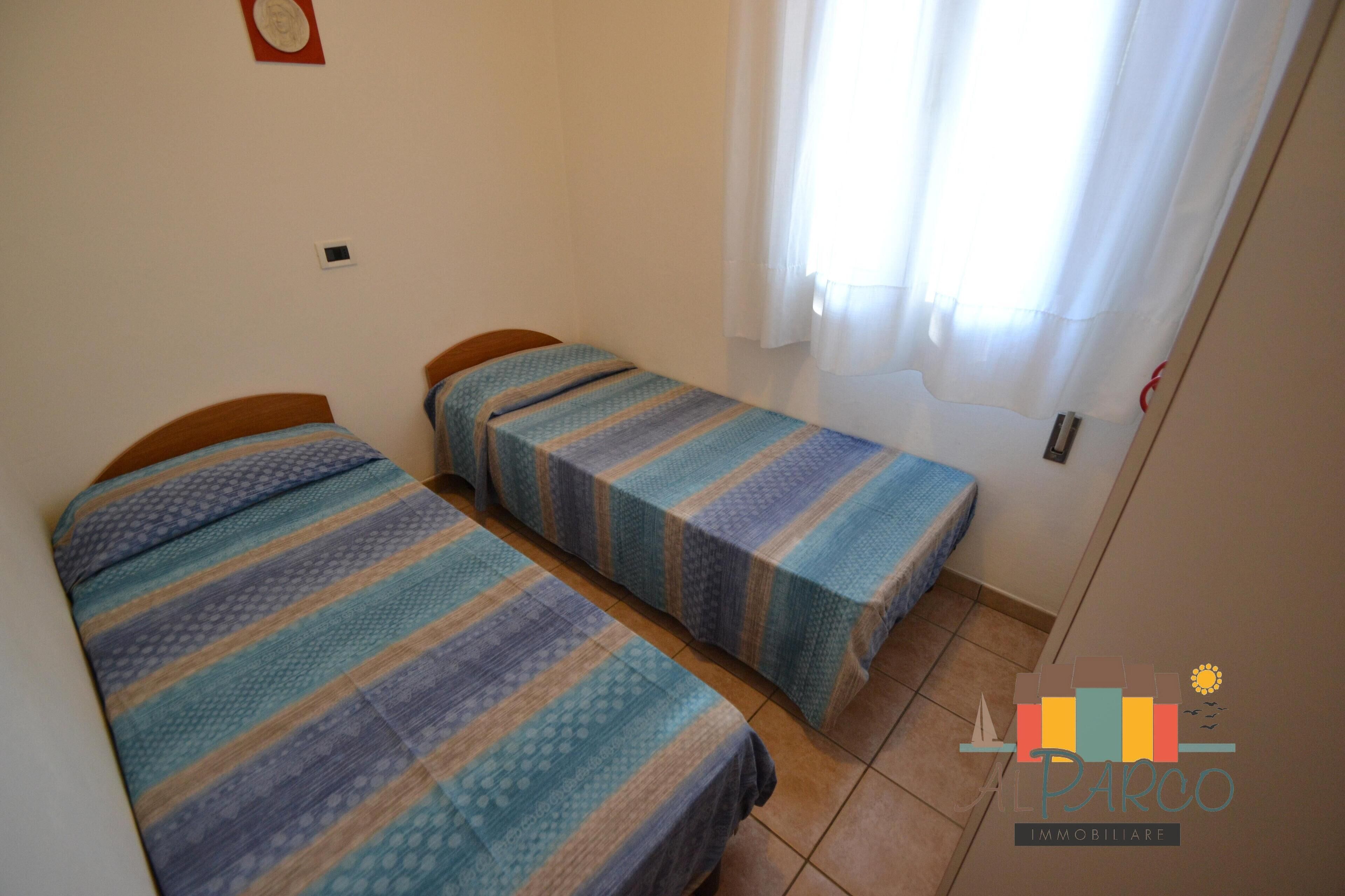 A small room with two single beds, a window with curtains, and a visible door.