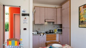Eine kompakte Küche mit Holzausstattung, einer Mikrowelle und einem Spülbecken. Ein Esstisch mit Tellern und einem Stuhl steht bereit.