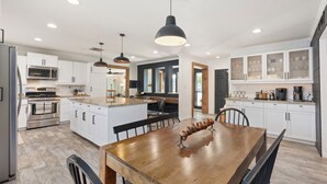 A modern kitchen with white cabinets, stainless steel appliances, and a wooden dining table.