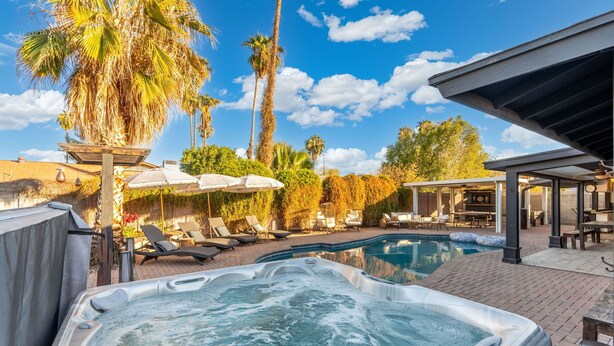 A hot tub and a pool area with lounge chairs and umbrellas.