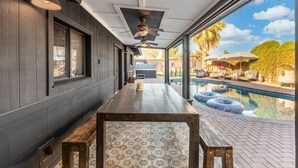 A covered outdoor area with a pool, wooden benches, and a table.