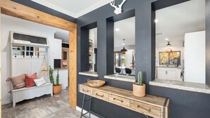 A modern interior with a wooden bench, a console table, and a mirror reflecting a kitchen area.