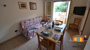 A cozy living area with a sofa, dining table set for two, and a television on a stand. - Apartment 2 bedrooms and pinewood view P2 42 (Rosolina Mare)