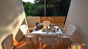 A balcony with a table set for four, surrounded by white chairs. There are various items on the table, including a box labeled "Alparco," a teapot, cups, and a bottle. - Apartment 2 bedrooms and pinewood view P2 42 (Rosolina Mare)
