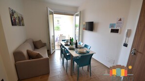 Un comedor con una mesa preparada para cuatro personas, un sofá y un televisor montado en la pared.