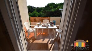 Een balkon met een tafel voor twee personen, een stoel en uitzicht op een groen landschap.