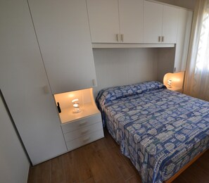 Un dormitorio con cama, lámparas de noche, armario y ventana con cortinas.