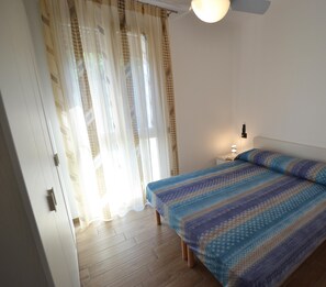 Un dormitorio con cama, cortinas, una mesita de noche y una lámpara fijada a la pared.