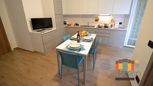 A modern kitchen with white cabinets, a dining table set for four, and a flat-screen TV mounted on the wall. - Apartment with 1 bedroom near to the beach LP 16 (Rosolina Mare)