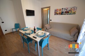 Un coin repas avec une table dressée pour quatre personnes, un canapé et un téléviseur fixé au mur.