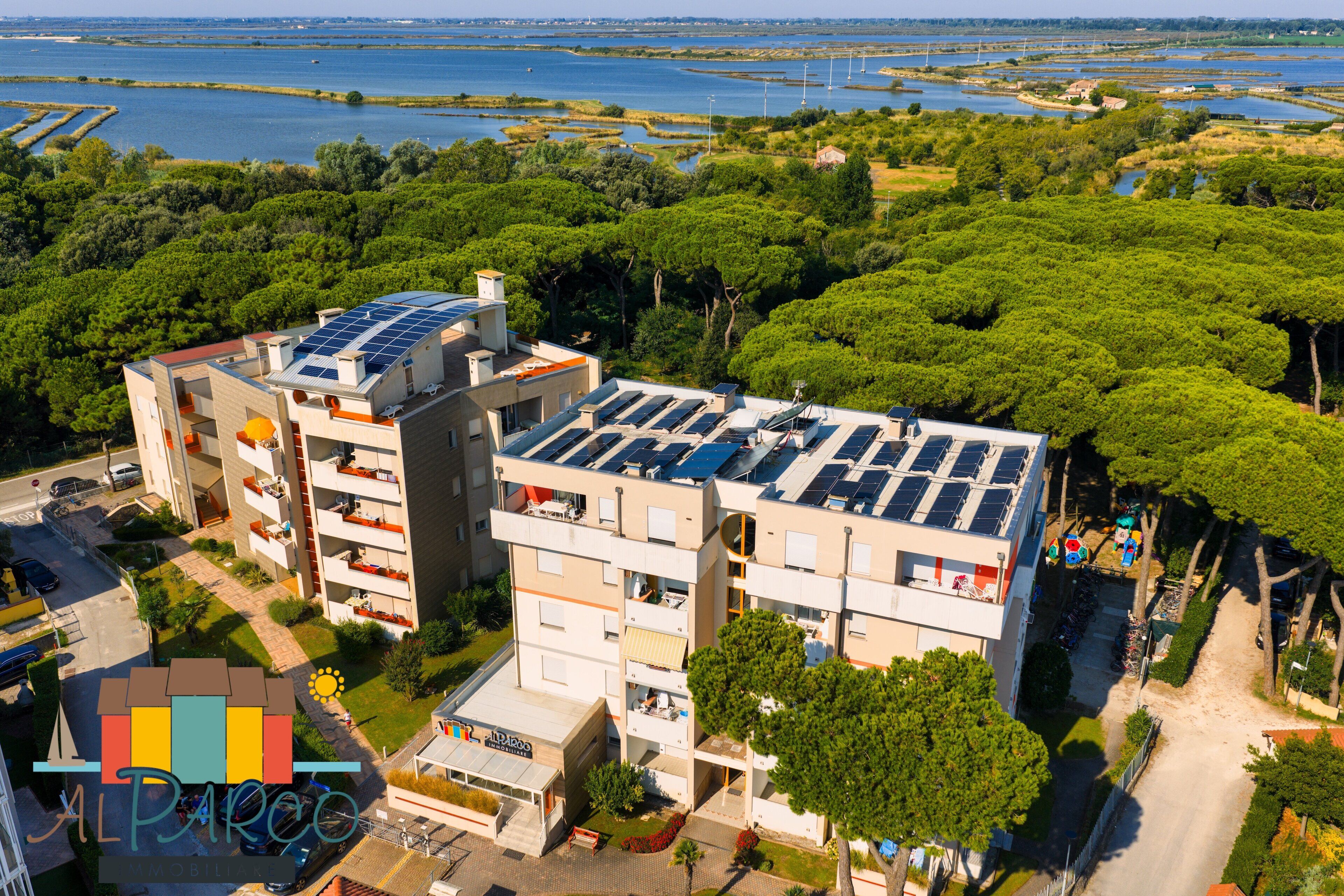 Un edificio de varios pisos con paneles solares en el techo, rodeado de vegetación y cuerpos de agua.