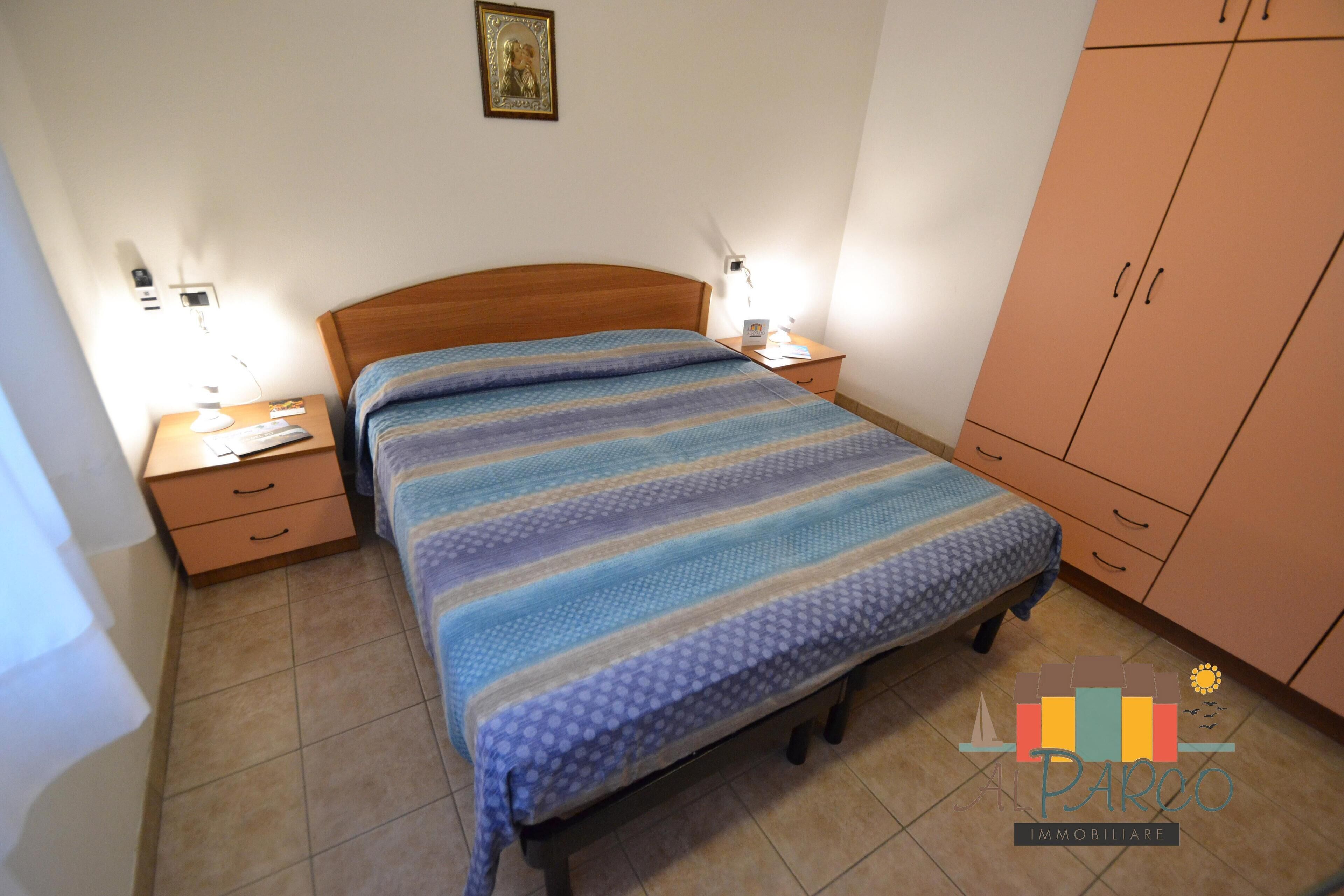 Un dormitorio con cama de madera, dos mesitas de noche, una cómoda y un cuadro enmarcado en la pared.