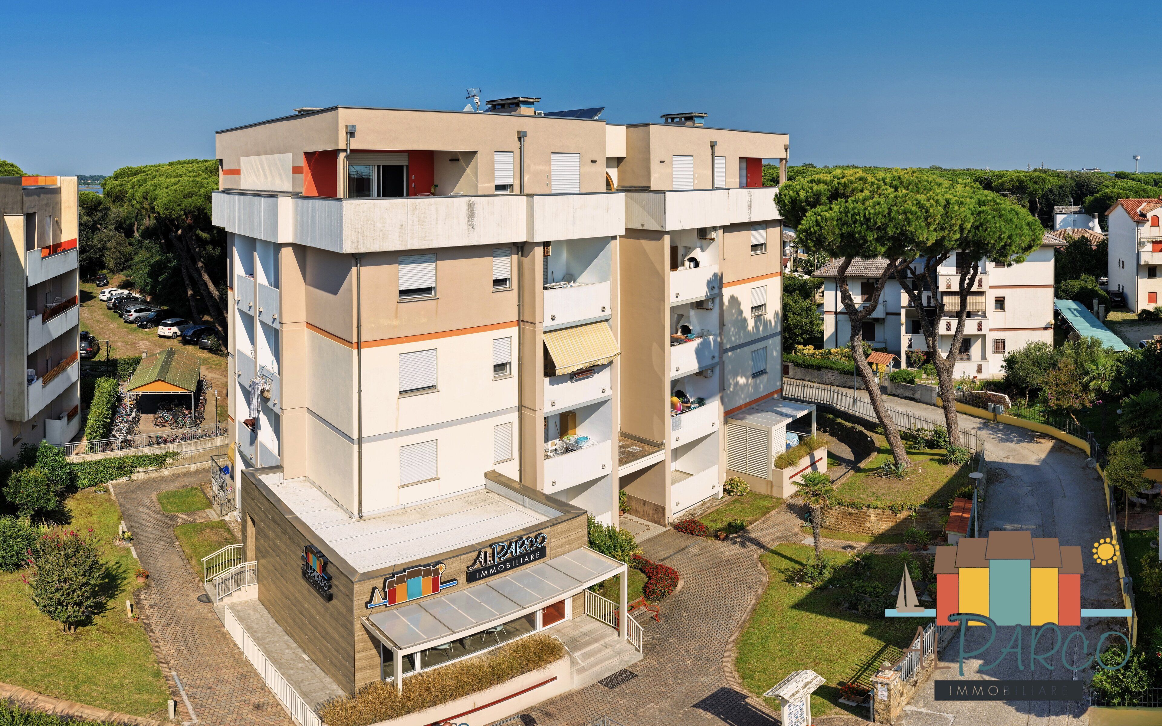 A multi-story building with a flat roof, a ground-level commercial space, and a parking area.