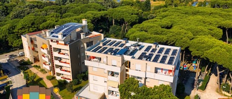 A multi-story building with solar panels on the roof, surrounded by greenery and water bodies.
