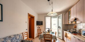 A compact kitchen with a dining area, a TV mounted on the wall, and a sofa in the living area. - Apartment 2 bedrooms near to the beach P 11 (Rosolina Mare)