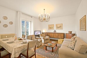 A living room with a dining area, a sofa, a television, and a chandelier.