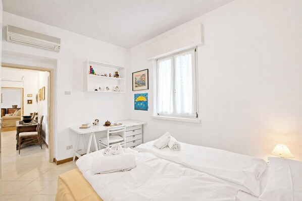 Een slaapkamer met een bed, een bureau, een stoel, een raam en een wandplank.
