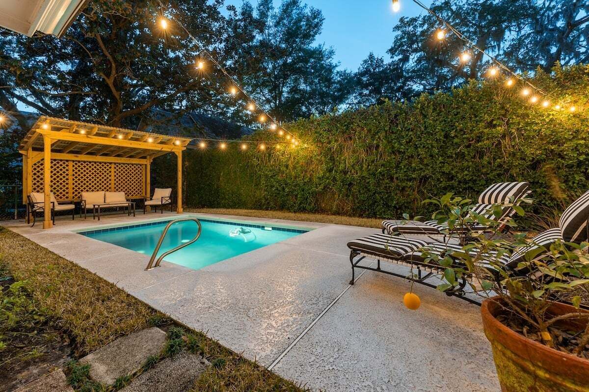 Un jardin avec une piscine, un espace salon couvert et des guirlandes lumineuses.