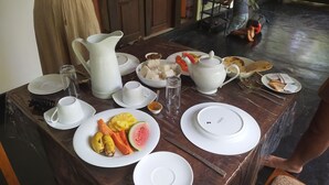 Una mesa de desayuno con platos de fruta, una jarrón, tazas y un bol de arroz.