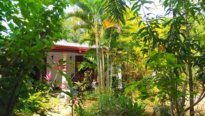 Un edificio tradicional con techo rojo, rodeado de abundante vegetación y diversas plantas.