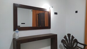 Un espejo con marco de madera, una botella de agua sobre una consola y una silla.