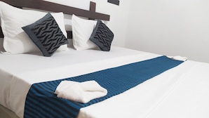 Una cama bien hecha con ropa de cama blanca, dos almohadas estampadas y una manta azul a rayas.