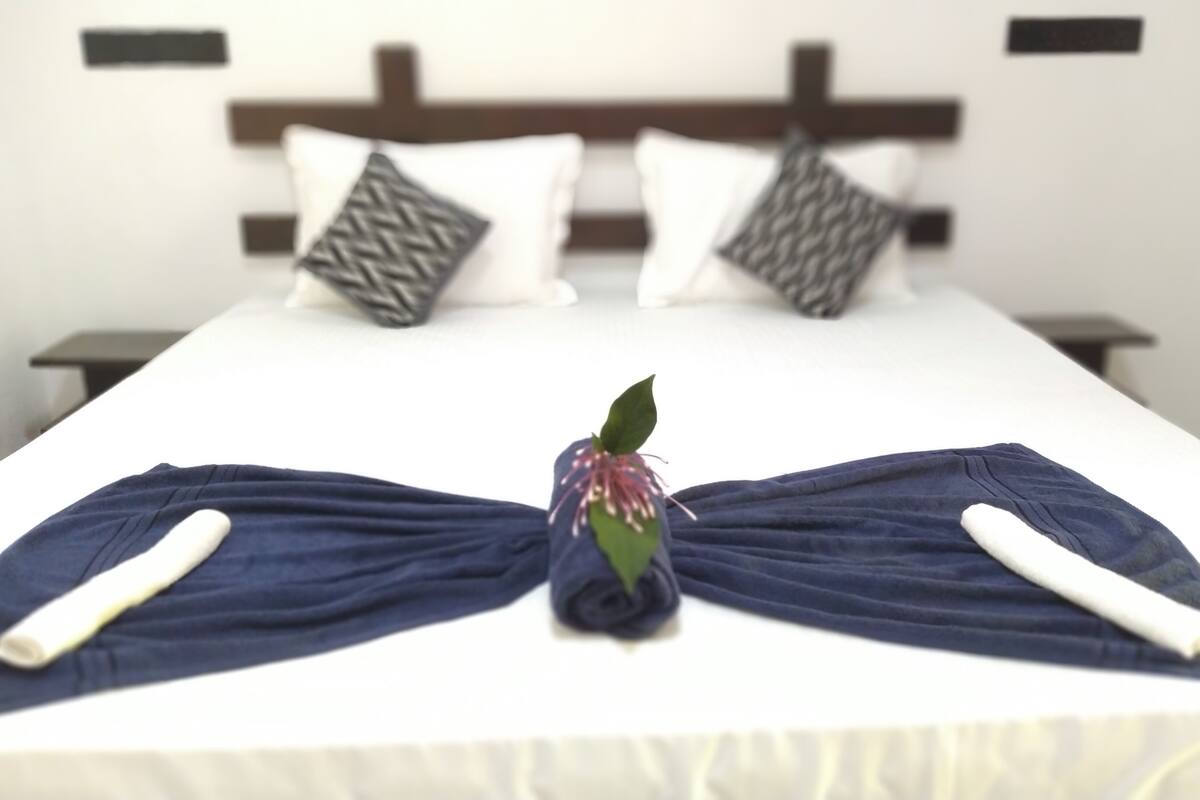 A neatly made bed with a decorative towel arrangement in the center, featuring a small plant.
