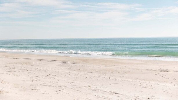 Ein Strand mit breitem Sandufer und sanften Wellen.